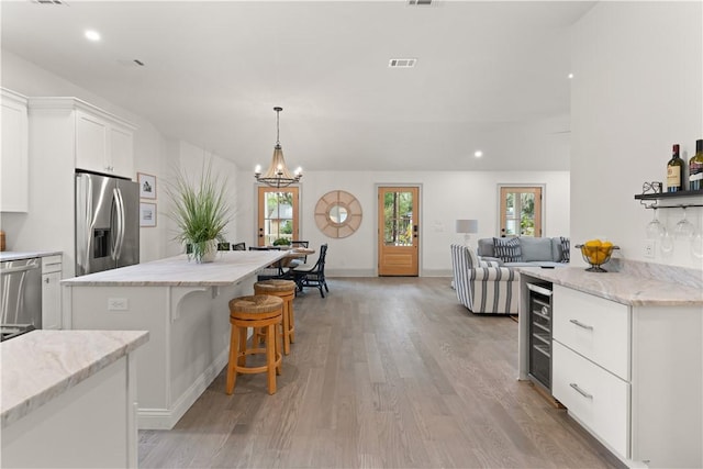 kitchen featuring stainless steel appliances, pendant lighting, a notable chandelier, white cabinets, and wine cooler