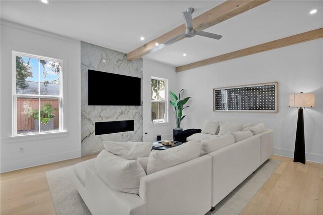 living room with ceiling fan, beam ceiling, a fireplace, and light hardwood / wood-style flooring