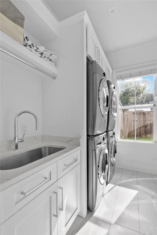 clothes washing area with cabinets, crown molding, stacked washer and clothes dryer, and sink