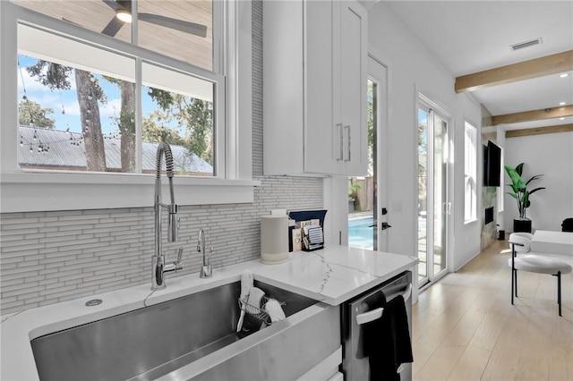 kitchen with white cabinets, sink, stainless steel dishwasher, decorative backsplash, and light stone counters