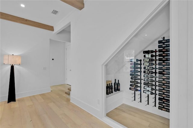 wine area with beam ceiling and light hardwood / wood-style floors