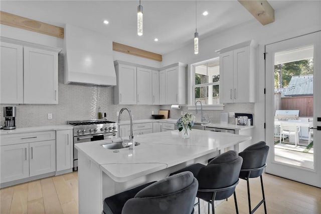 kitchen featuring white cabinetry, hanging light fixtures, a kitchen island with sink, high end range, and custom range hood