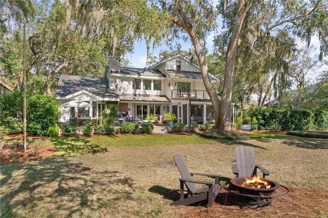 back of property featuring a balcony, a standing seam roof, a fire pit, a lawn, and metal roof