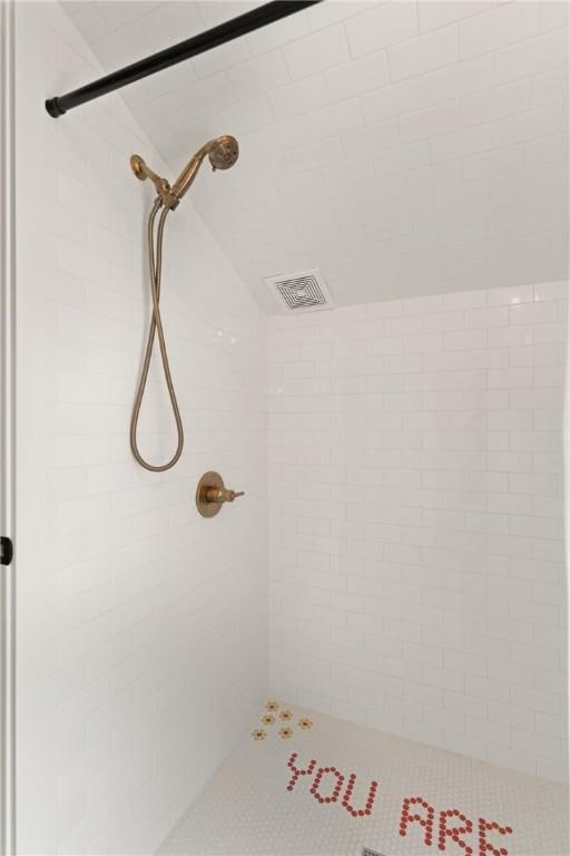 bathroom with visible vents, tiled shower, and lofted ceiling