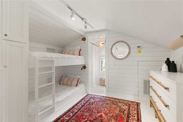 unfurnished bedroom with visible vents, wooden walls, rail lighting, and vaulted ceiling