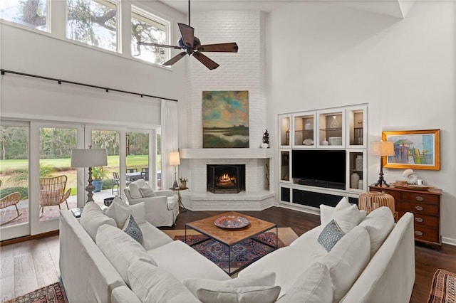 living room with a towering ceiling, a brick fireplace, wood finished floors, and a ceiling fan