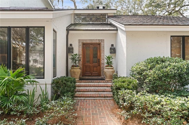 entrance to property featuring a shingled roof and stucco siding