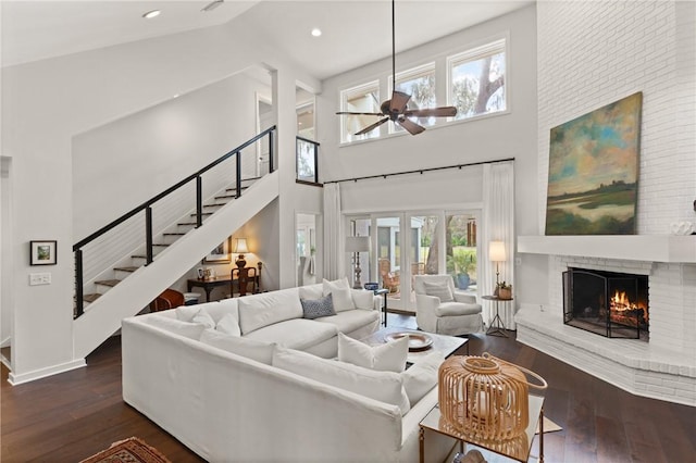 living area with stairway, a brick fireplace, ceiling fan, and hardwood / wood-style floors