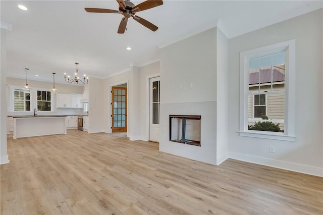 unfurnished living room with light hardwood / wood-style flooring, ceiling fan with notable chandelier, and sink