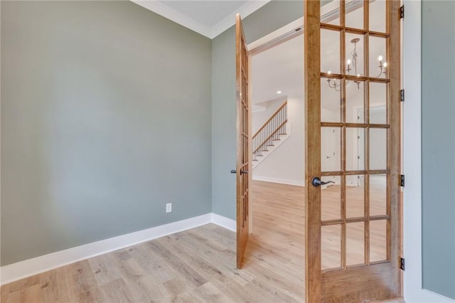 spare room with french doors, light hardwood / wood-style floors, an inviting chandelier, and crown molding