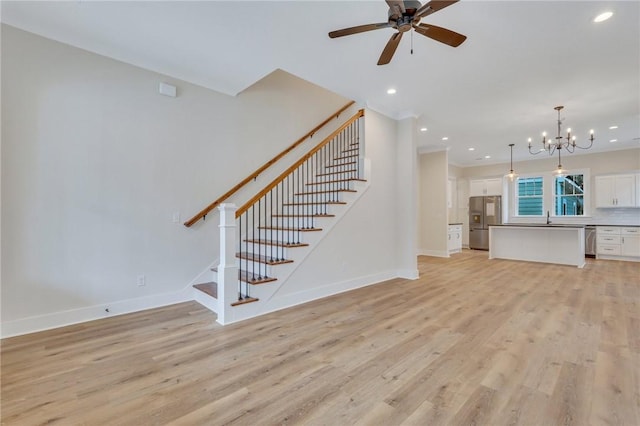 unfurnished living room with light hardwood / wood-style flooring, ceiling fan with notable chandelier, and sink