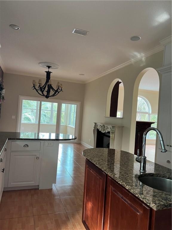 kitchen featuring a fireplace, white cabinetry, sink, dark stone counters, and ornamental molding