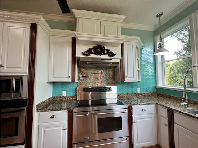 kitchen with crown molding, dark stone countertops, white cabinets, stainless steel appliances, and backsplash