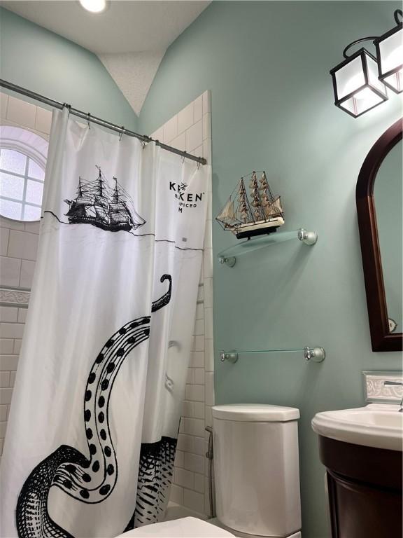 bathroom with a shower with curtain, vanity, vaulted ceiling, and toilet