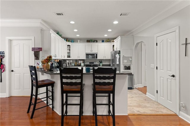 kitchen with a breakfast bar, white cabinets, light hardwood / wood-style flooring, appliances with stainless steel finishes, and kitchen peninsula