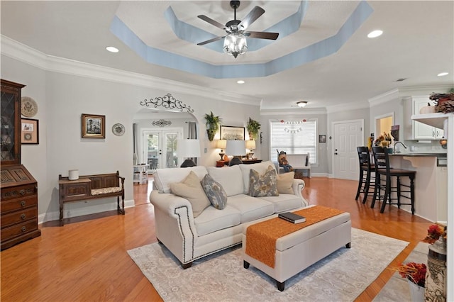 living room with ceiling fan, french doors, crown molding, light hardwood / wood-style floors, and a tray ceiling