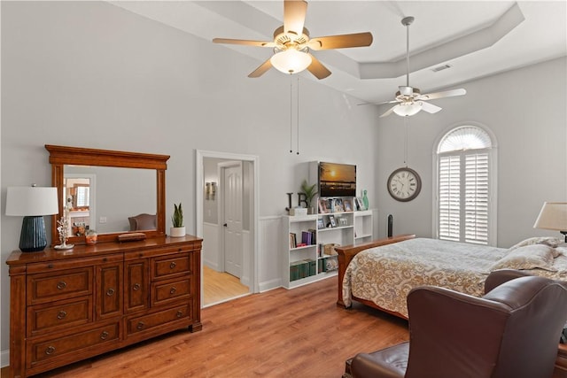 bedroom with light hardwood / wood-style floors, a raised ceiling, and ceiling fan