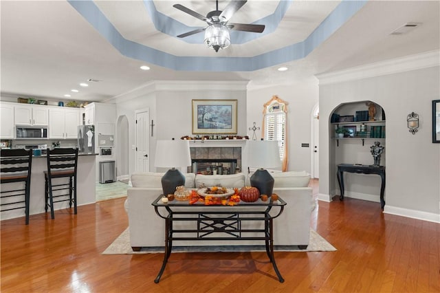 living room with a raised ceiling, a tiled fireplace, crown molding, and dark hardwood / wood-style flooring