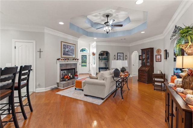 living room featuring a tray ceiling, ceiling fan, crown molding, a fireplace, and light hardwood / wood-style floors