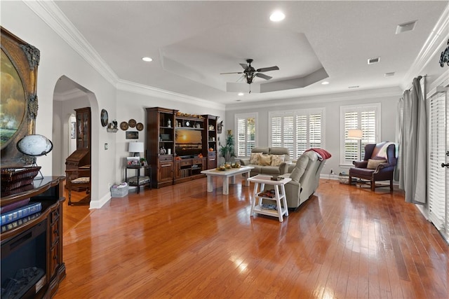 living room featuring hardwood / wood-style flooring, a raised ceiling, ceiling fan, and crown molding