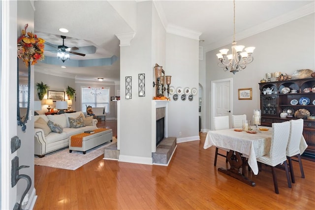 dining room featuring hardwood / wood-style floors, ceiling fan with notable chandelier, crown molding, and a tiled fireplace