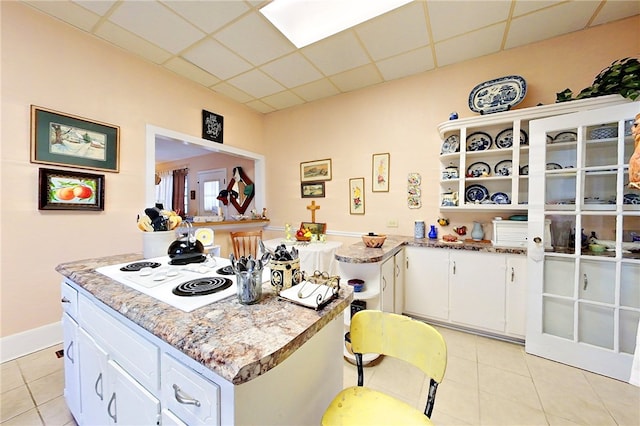 kitchen featuring white cabinetry, a paneled ceiling, white electric cooktop, light tile patterned floors, and light stone countertops