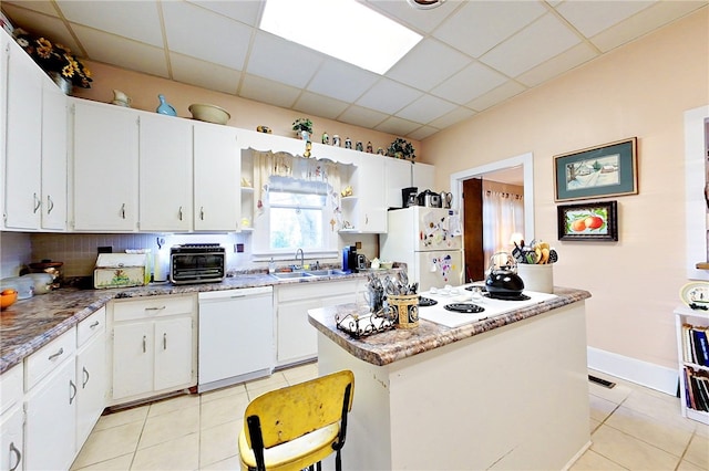 kitchen with sink, white appliances, a paneled ceiling, a center island, and white cabinets