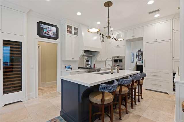 kitchen featuring pendant lighting, a kitchen island with sink, sink, white cabinetry, and beverage cooler