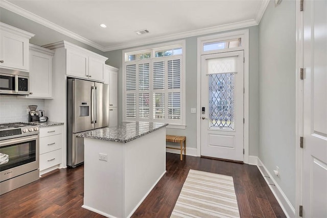 kitchen with appliances with stainless steel finishes, light stone counters, dark wood-type flooring, white cabinets, and a kitchen island