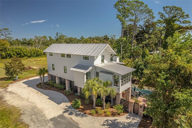 10 Fern Ln, Saint Simons Island, GA 31522 - view of front of home with driveway, a sunroom, a metal roof, and view of wooded area