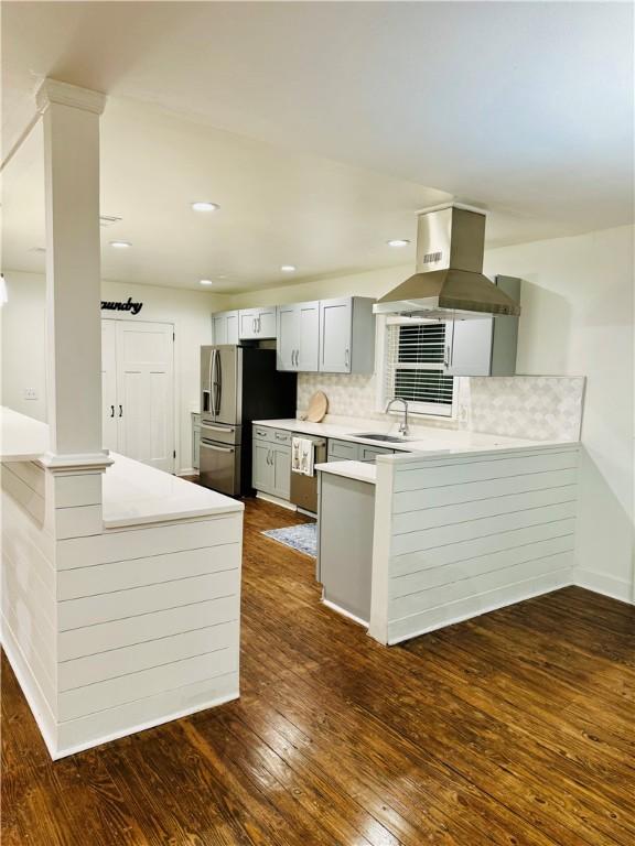 kitchen featuring dark hardwood / wood-style flooring, backsplash, kitchen peninsula, island range hood, and appliances with stainless steel finishes