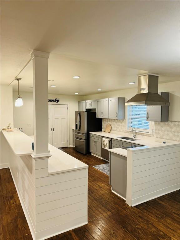 kitchen with kitchen peninsula, island range hood, dark wood-type flooring, sink, and pendant lighting