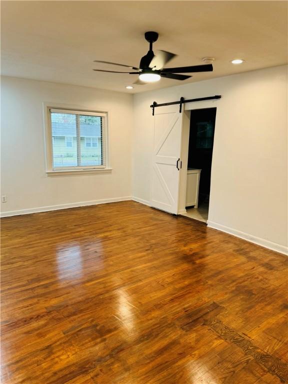 unfurnished room featuring hardwood / wood-style flooring, ceiling fan, and a barn door