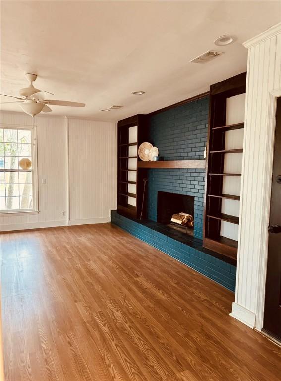 unfurnished living room with hardwood / wood-style flooring, ceiling fan, built in features, and a brick fireplace