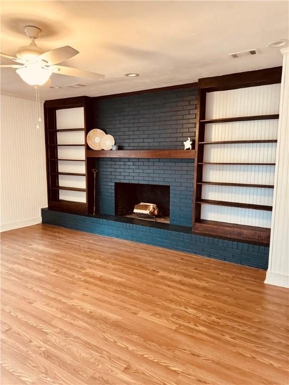 unfurnished living room featuring ceiling fan, light wood-type flooring, and a brick fireplace