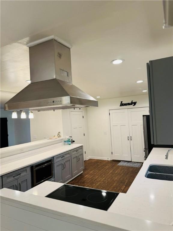 kitchen with gray cabinetry, black electric cooktop, island range hood, dark wood-type flooring, and sink