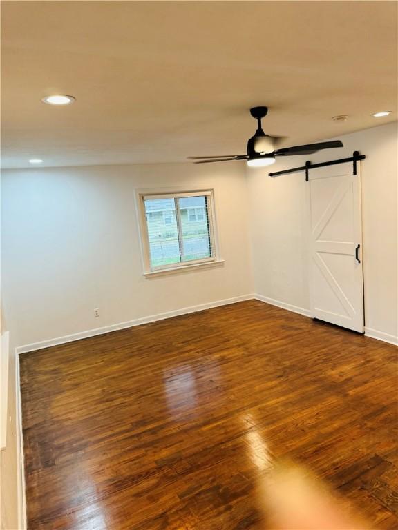 unfurnished room featuring a barn door, ceiling fan, and dark hardwood / wood-style flooring