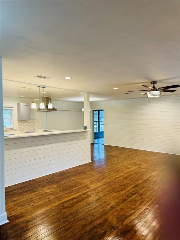 unfurnished living room featuring ceiling fan with notable chandelier and dark hardwood / wood-style floors