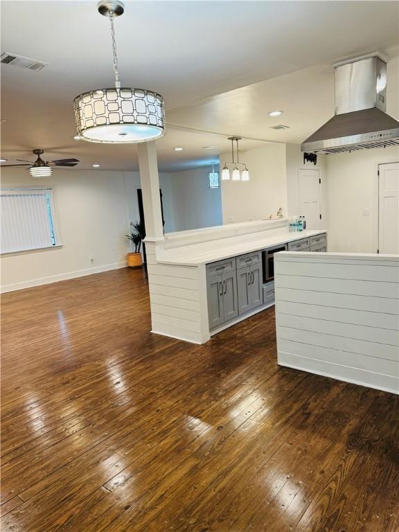 kitchen featuring wall chimney exhaust hood, gray cabinetry, ceiling fan, pendant lighting, and dark hardwood / wood-style floors