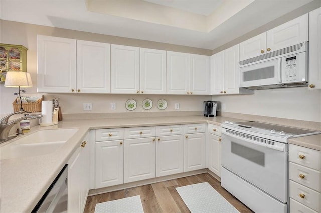 kitchen featuring sink, light hardwood / wood-style flooring, a tray ceiling, white appliances, and white cabinets