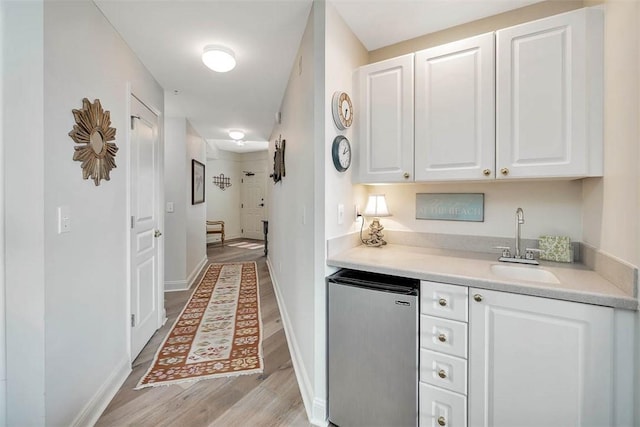 bar with sink, light hardwood / wood-style floors, white cabinets, and refrigerator