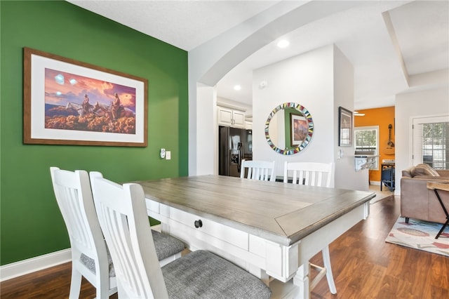 dining area with baseboards, arched walkways, and wood finished floors