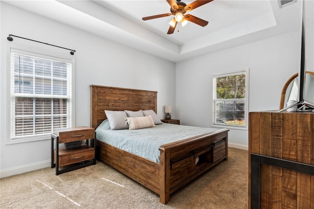 bedroom with baseboards, visible vents, a tray ceiling, and light colored carpet