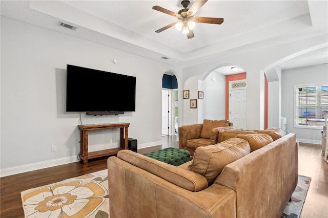 living area with baseboards, visible vents, arched walkways, wood finished floors, and a tray ceiling