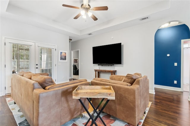 living room featuring a tray ceiling, arched walkways, visible vents, wood finished floors, and baseboards