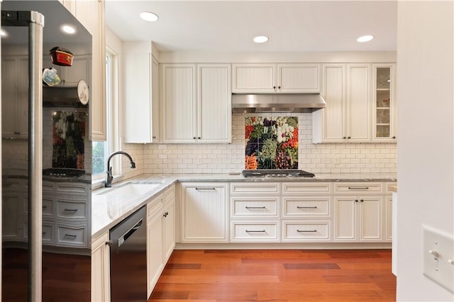 kitchen featuring dishwasher, light stone countertops, under cabinet range hood, stainless steel gas cooktop, and a sink