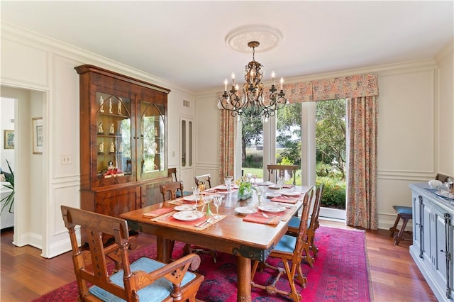 dining space with crown molding, dark wood-style flooring, a chandelier, and a decorative wall