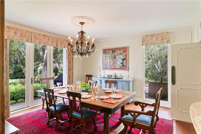 dining room featuring ornamental molding, a healthy amount of sunlight, a decorative wall, and wood finished floors