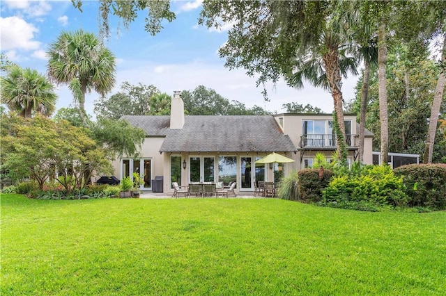 rear view of property featuring a chimney, a lawn, a patio, and stucco siding