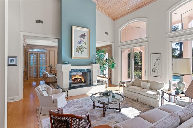 living room featuring crown molding, a towering ceiling, a fireplace, light hardwood / wood-style floors, and wood ceiling